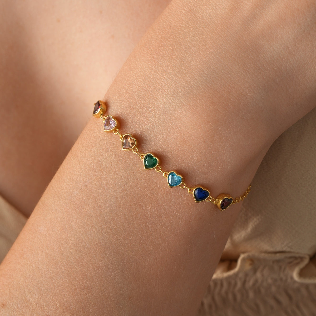 Gold vermeil heart birthstone bracelet with seven colourful stones, shown close up on the wrist.