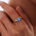 Square close-up of an oval blue birthstone ring with ribbed gold vermeil shoulders worn on a finger