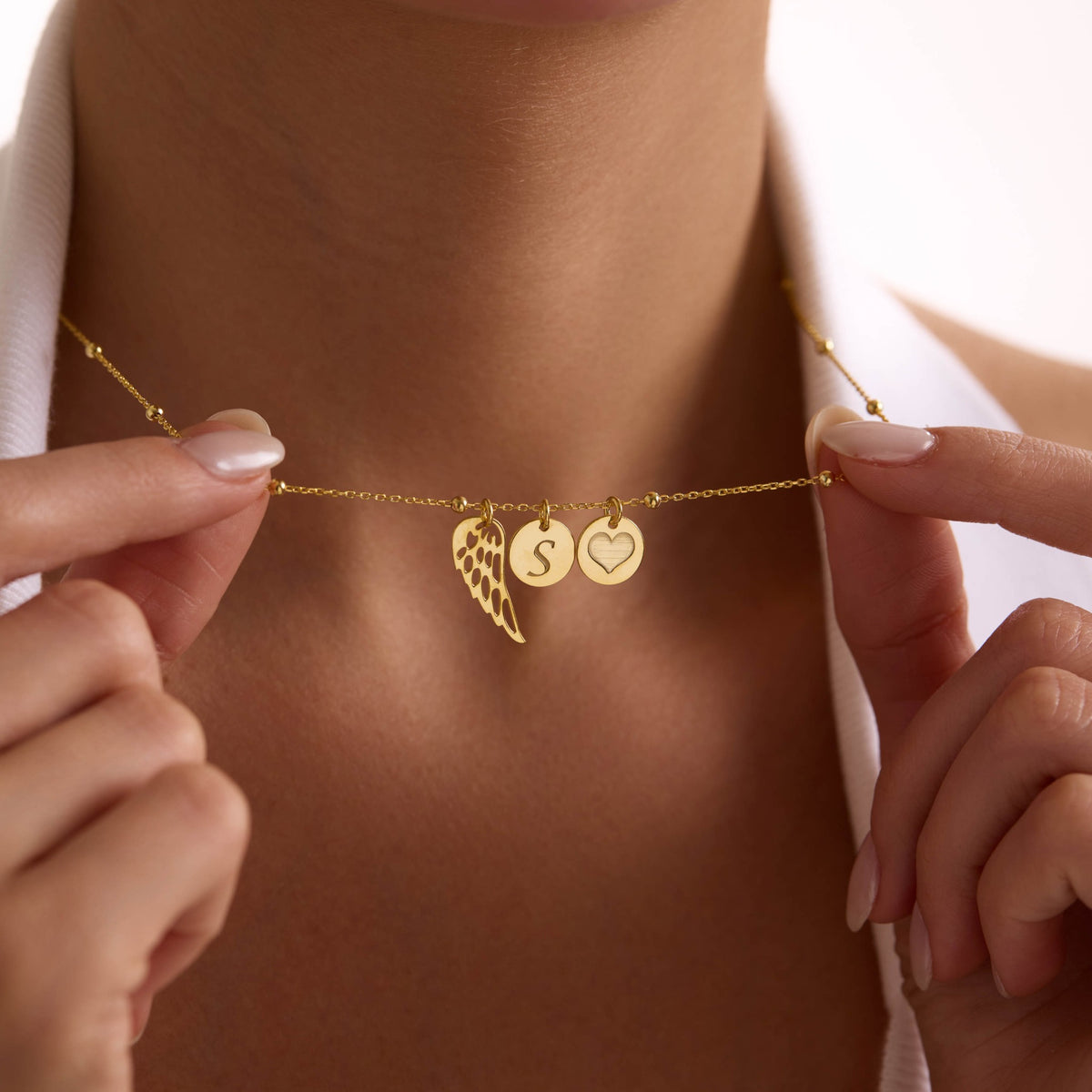 Gold vermeil angel wing necklace on a satellite chain with personalised S and heart discs shown close up.