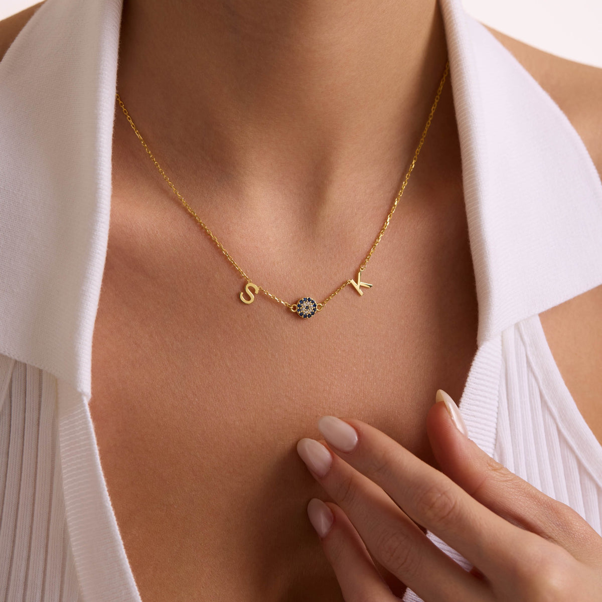 Personalised gold S and K initial necklace with a blue evil eye, styled with an open white shirt.