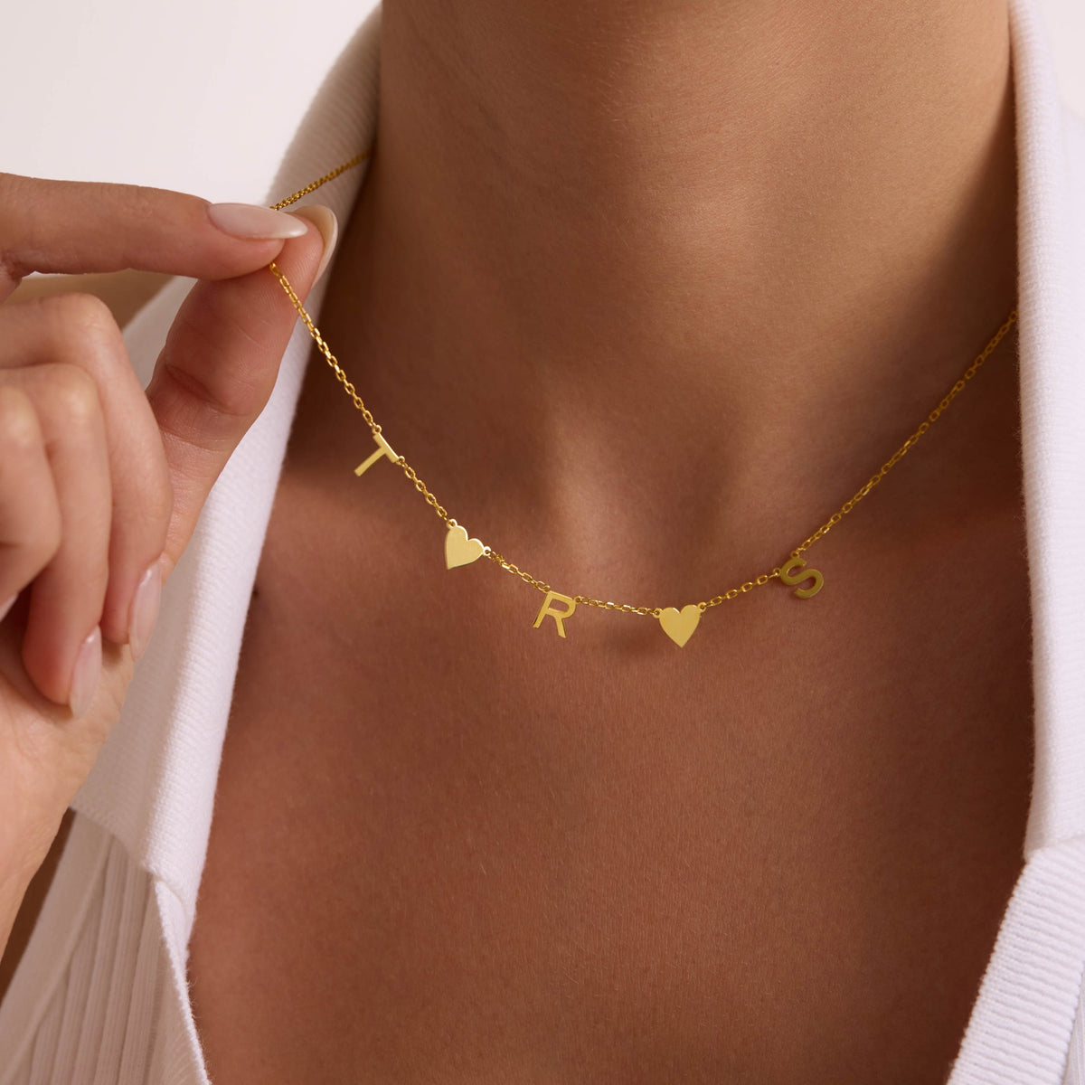 Close view of a personalised gold T, R and S letter necklace with two heart charms.