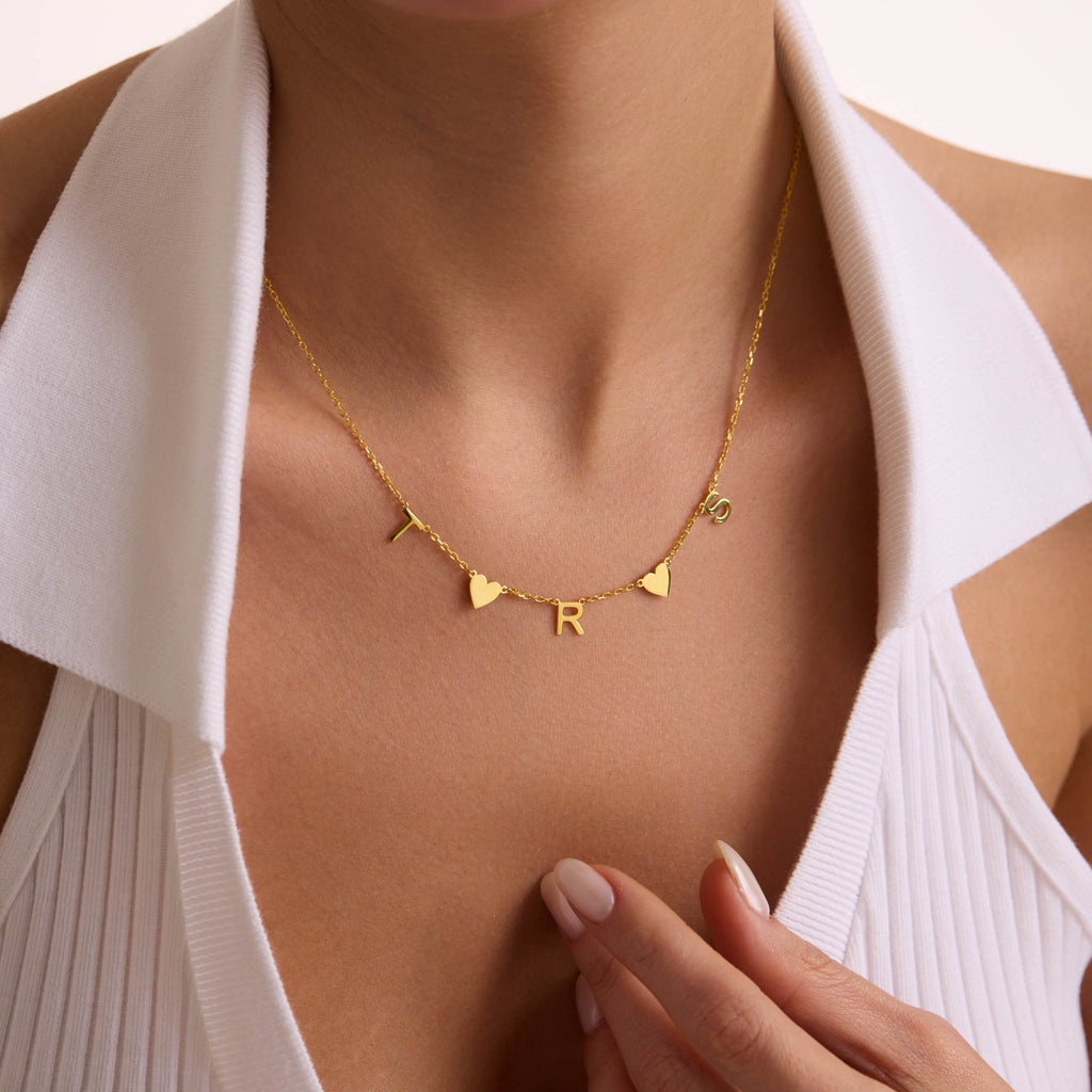 Personalised gold T, R and S initial necklace with heart charms, styled against a white shirt.