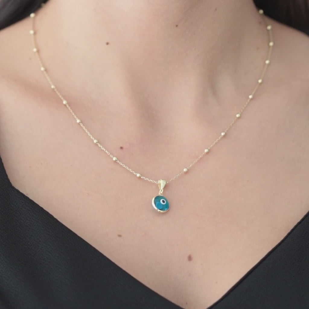 Blue evil eye pendant on a gold vermeil satellite chain, shown worn at the neckline.