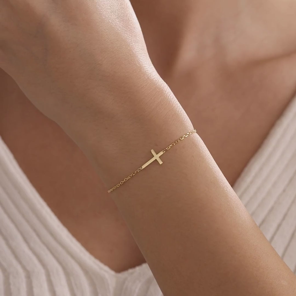 Dainty cross bracelet in gold vermeil, showing a polished sideways cross on a delicate chain worn on the wrist.