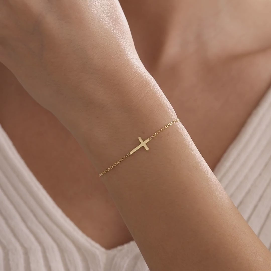 Dainty cross bracelet in gold vermeil, showing a polished sideways cross on a delicate chain worn on the wrist.