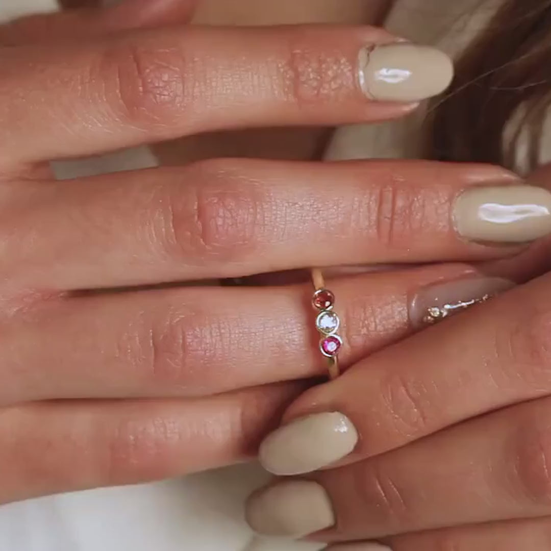 Personalised family birthstone ring with three round coloured stones, worn on a hand