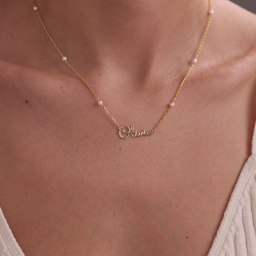 Personalised name necklaces worn at the neckline: Olivia on a gold pearl satellite chain, Amelia on a gold satellite chain, and Samuel on a silver paperclip chain.