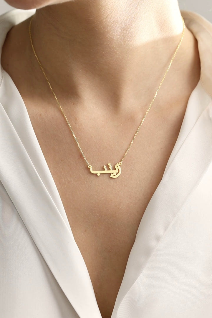 Personalised Arabic name necklace in 14K gold vermeil over sterling silver, showing Arabic lettering worn and held close up.