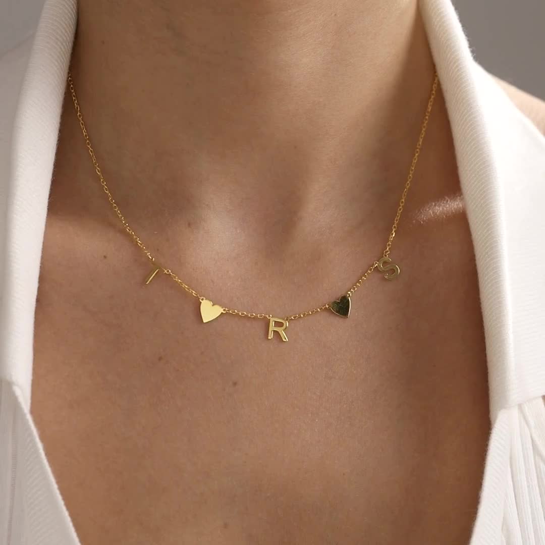 Personalised initial necklace in gold vermeil, showing a heart charm design first, followed by initials with a blue evil eye, worn at the neckline.