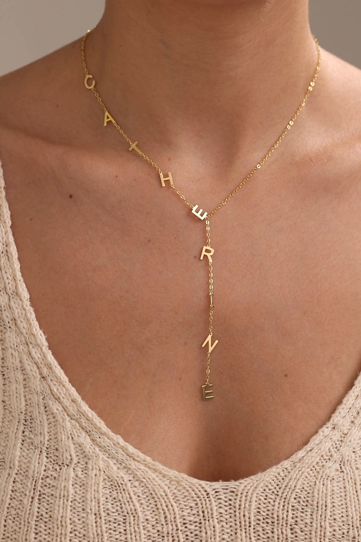 Personalised vertical name necklace with individual letters along a lariat chain, shown in gold and silver finishes while worn.